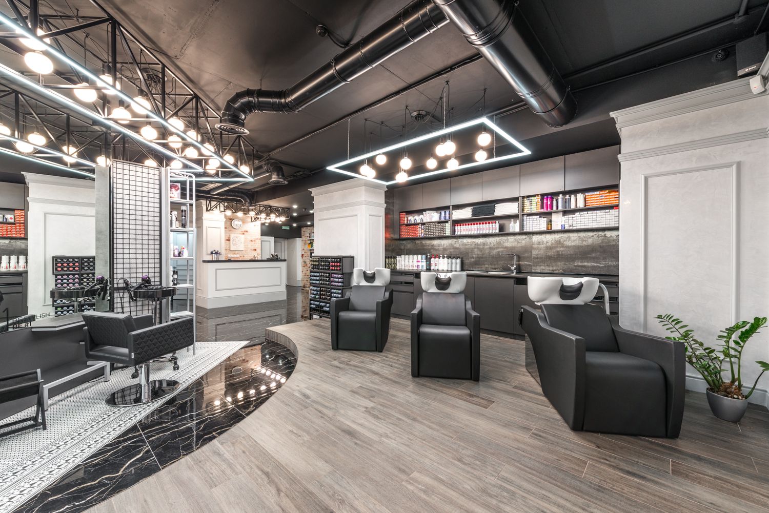 Le salon : fauteuils noirs, bacs de lavage et suspensions lumineuses